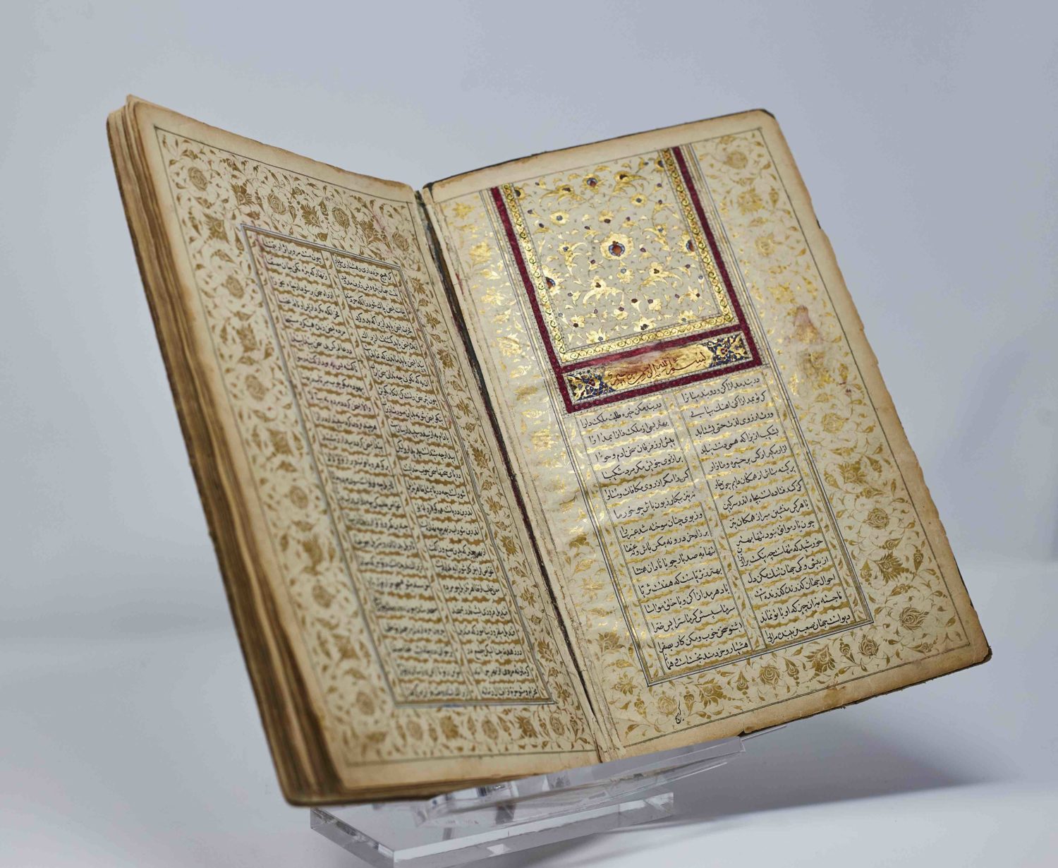 An old and delicate-looking book filled with gold design and Arabic calligraphy.