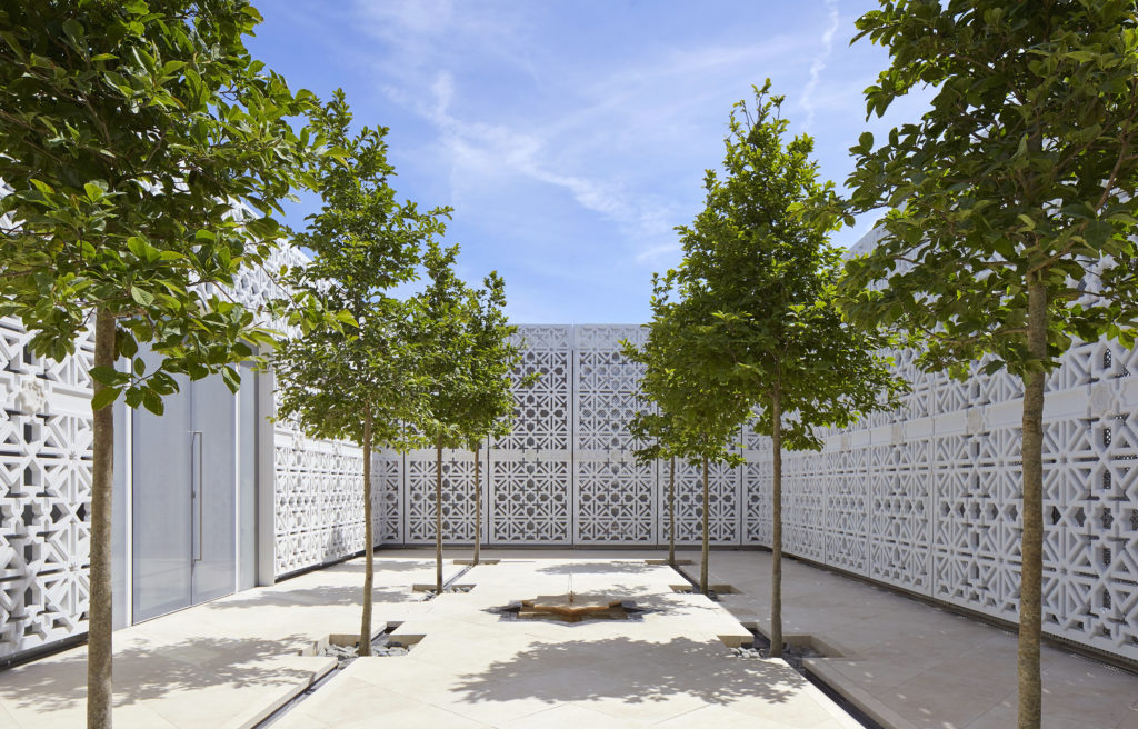 The Garden of Light - a garden with white, stone, carved walls and magnolia trees with a small fountain in the centre.