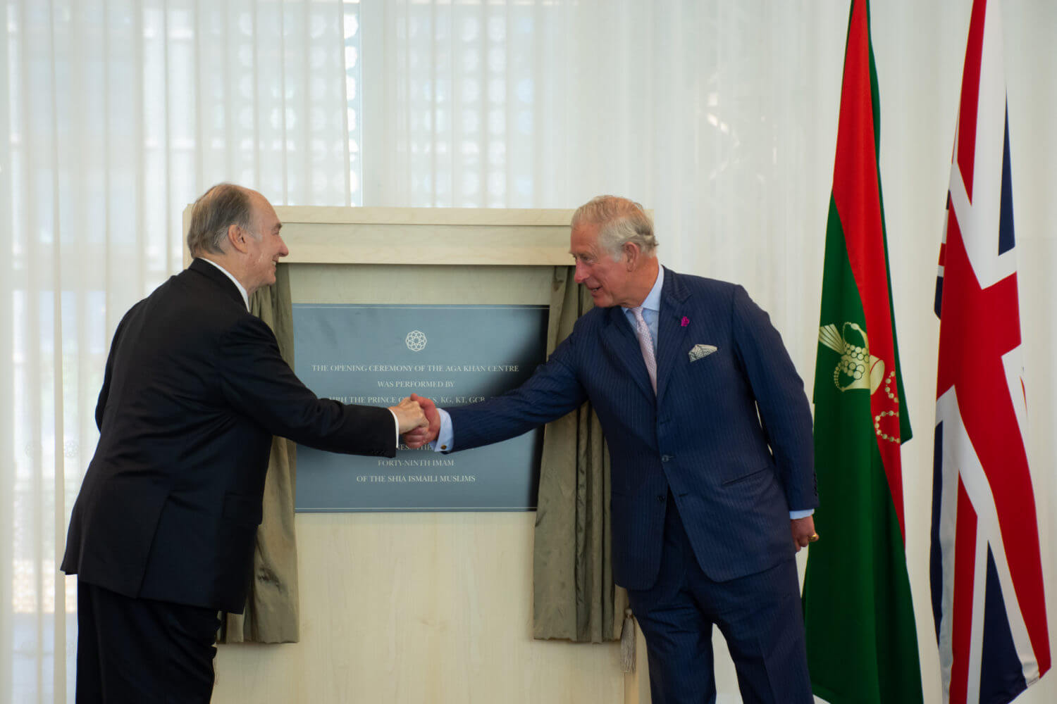 His Late Highness Aga Khan IV shaking hands with King Charles III next to an opening plaque.