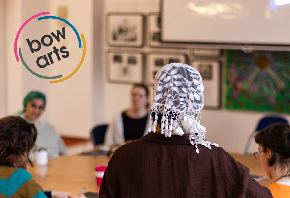 A group of people around a circular table with a bow arts logo in the corner.
